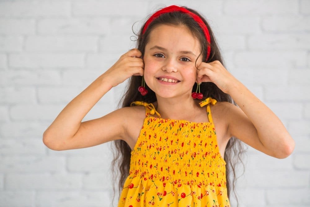 smiling cute girl holding cherries near ear like earrings